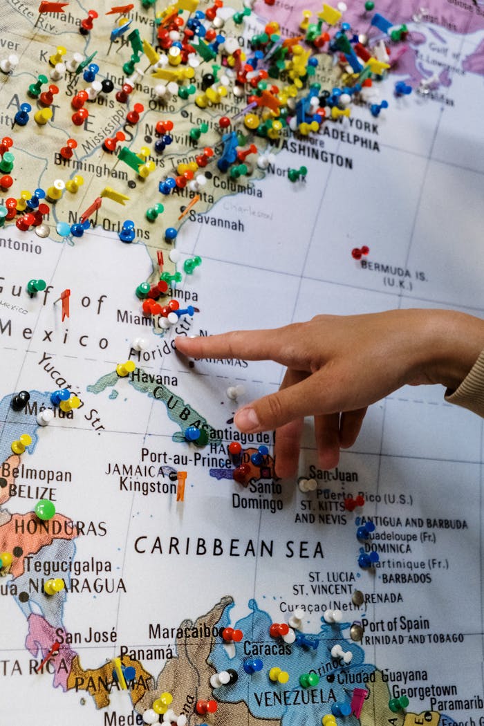 A close-up of a hand pointing at a map filled with colorful pins indicating travel destinations.